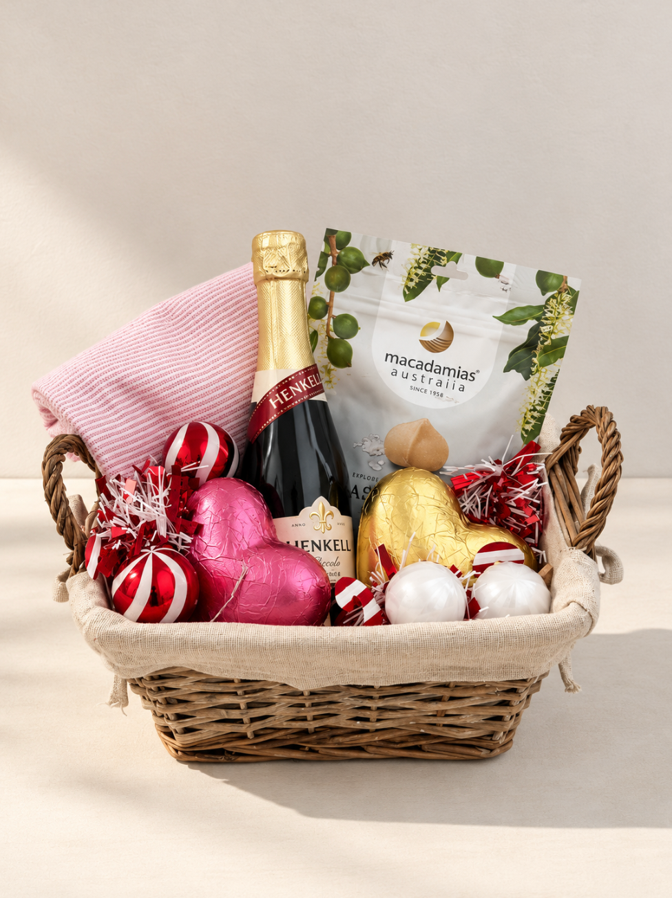 Hamp It Up x Kemeny’s Henkell Piccolo Christmas gift basket with Henkell sparkling wine, Macadamias Australia, pink and gold chocolate hearts and striped tea towel in a linen-lined wicker basket