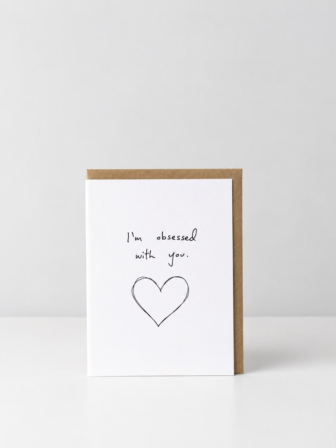 See Aiche greeting card reading “I’m obsessed with you.” above a hand-drawn heart outlined several times, with a kraft envelope